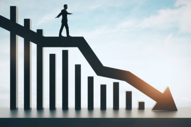 istock Backlit businessman balancing on abstract black downward chart arrow on light sky with clouds and mock up place background. Down, drop, finance and crisis concept. 1386725465
