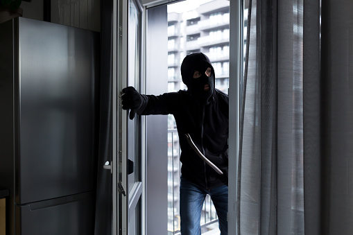 Un ladrón masculino con una máscara negra, entra en el apartamento para robar, el ladrón rompió la cerradura de la puerta photo