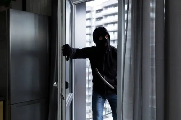 Photo of A male thief in a black mask, enters the apartment for robbery, the robber broke the door lock