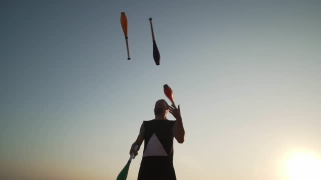 Juggler man throwing clubs against blue sky shaky footage slow motion