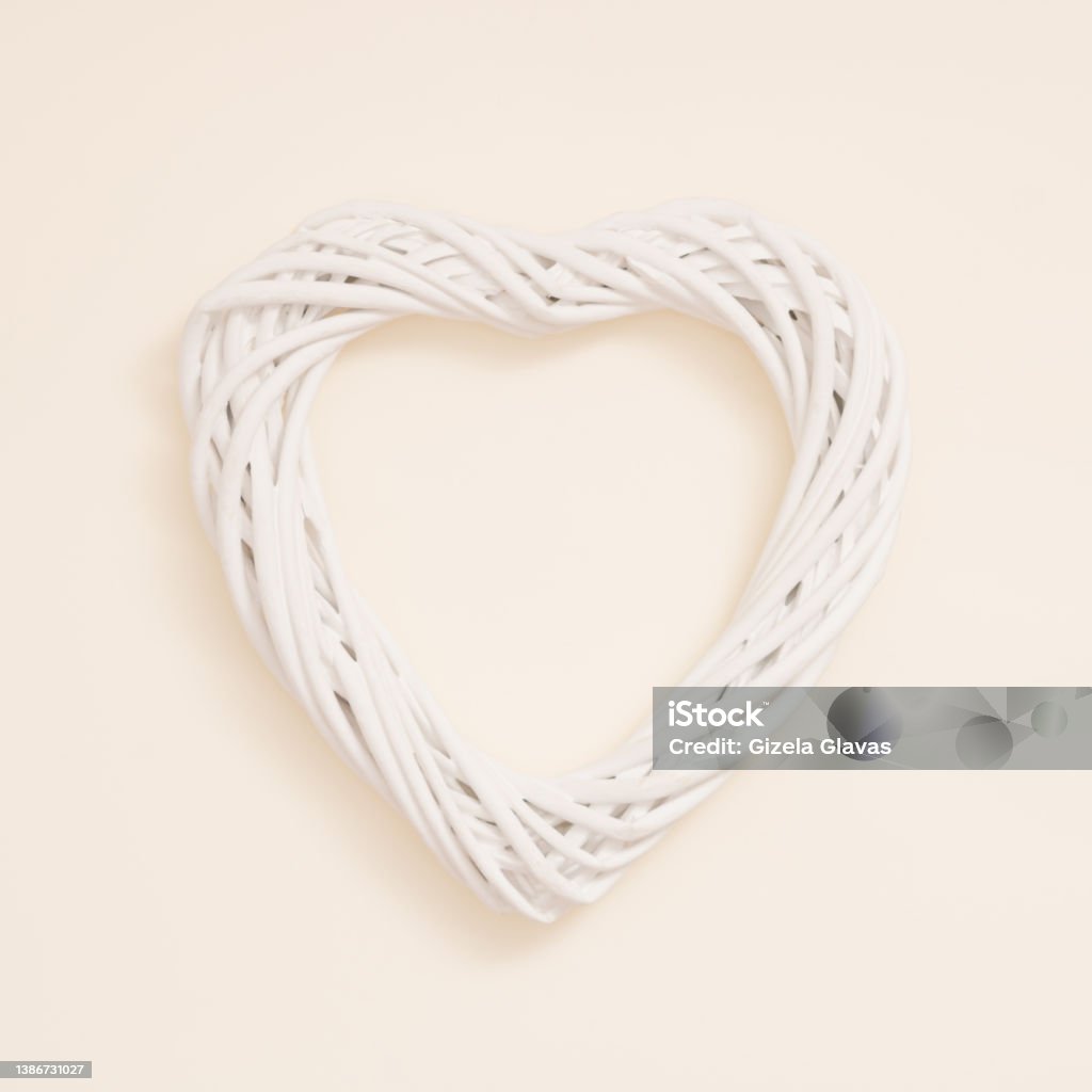 A heart made of knitted white wicker on a pastel beige background. Minimal creative concept of decorative infatuation, love, Valentine's Day, weddings. Heart Shape Stock Photo