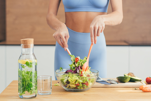 Close up photo, body part, hands of young fitness woman making salad with fresh vegetables and fresh detox drink in kitchen at home