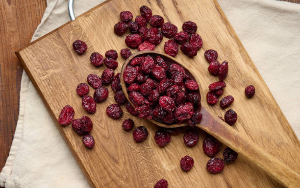 manojo de arándanos secos en una cuchara de madera sobre una mesa marrón. deliciosa baya, vista superior - dried cranberry fotografías e imágenes de stock