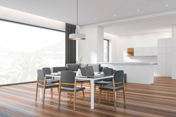 istock Modern dining room interior, panoramic window, large glass table with chairs. Stylish kitchen. hardwood flooring. Laptop. Couch. White open space area. 3d rendering. 1386739246