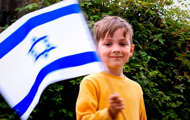 lächelnder kaukasischer junge, der eine israelische flagge schwenkt und in die kamera schaut - israel judaism israeli flag flag stock-fotos und bilder