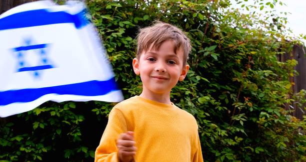 lächelnder kaukasischer junge, der eine israelische flagge schwenkt und in die kamera schaut - israel judaism israeli flag flag stock-fotos und bilder