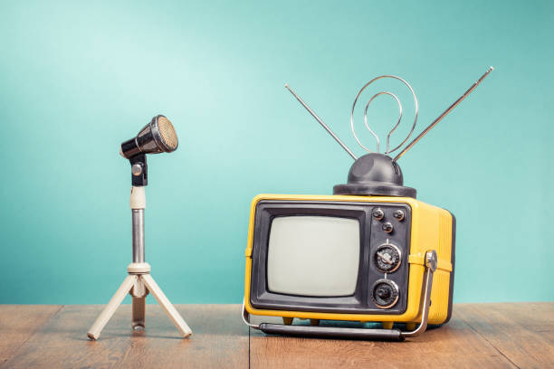 istock Retro old outdated yellow TV receiver from circa 80s and microphone on wooden table front mint green wall background. Vintage style filtered photo 1386744029