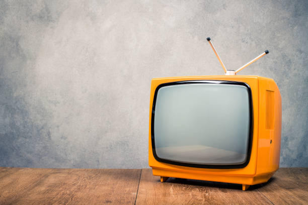 istock Retro old orange TV receiver on table front textured concrete wall background. Vintage style filtered photo 1386752164