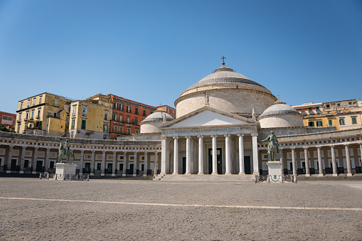 View of Basilica Reale Pontificia San Francesco da Paola church on Piazza del Plebiscito, main square of the city, and stone lion sculptures in Naples, Italy.