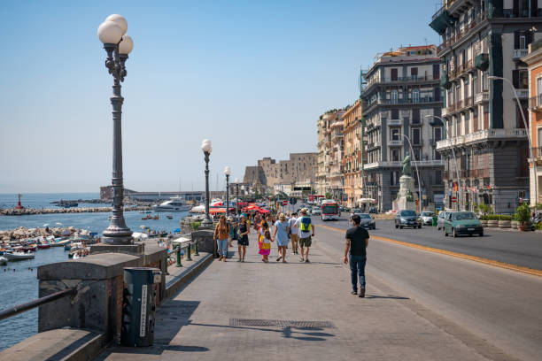 Tourists walking at Via Partenope Promenade in Napoli, Italy. People taking sun over sea rocks. stock photo