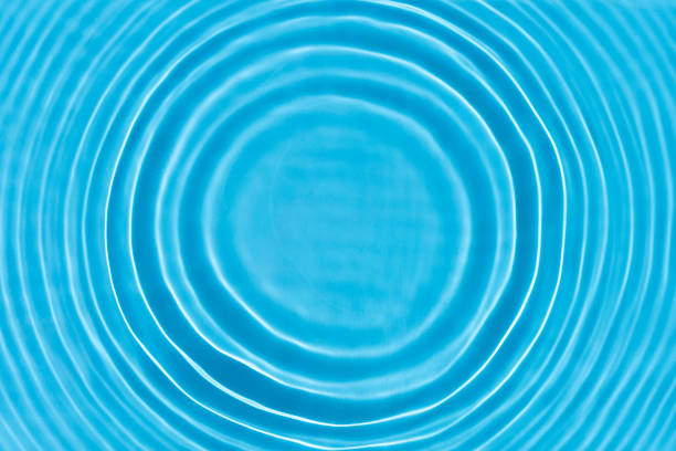 Wave from a drop of water on blue water under natural light. Top view, flat lay.