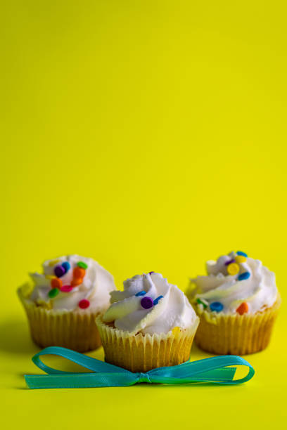 istock Three white frosting, colorful sprinkles cupcakes with light blue bowtie on bright greenish yellow background. 1386754981