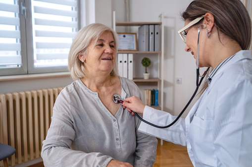 Beautiful doctor examines senior woman heartbeat at the doctor's office