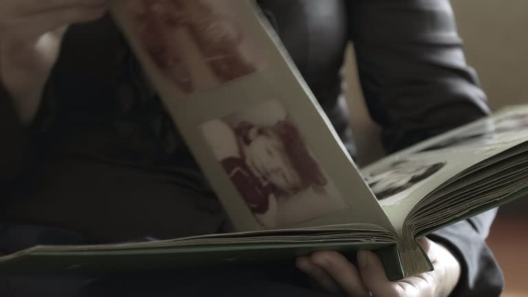 Woman is looking at old photo album at home and recalls the past. Watching through retro photographs of her family. Concept of biography, history, nostalgia and memories of youth, childhood, remembering, relatives. Close-up