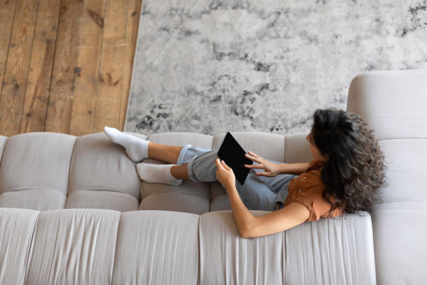 istock Top view of young woman with tablet computer sitting on sofa, working or studying online from home, mockup for app 1386755942