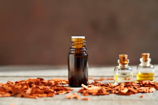 uma garrafa de óleo essencial de sândalo com lascas de sândalo vermelho em uma mesa - aromatherapy oil massage oil alternative therapy massaging - fotografias e filmes do acervo