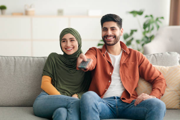 istock Cheerful Arabic Spouses Watching Television Switching Channels Sitting At Home 1386758944