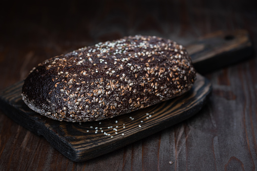 Whole rye bread covered with hemp seeds on the old wooden board