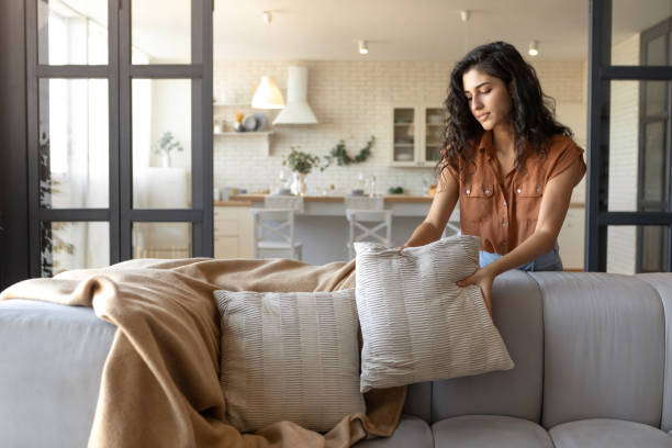 istock Attractive young woman arranging pillows and plaid on comfortable sofa, making her home cozy, empty space 1386760404