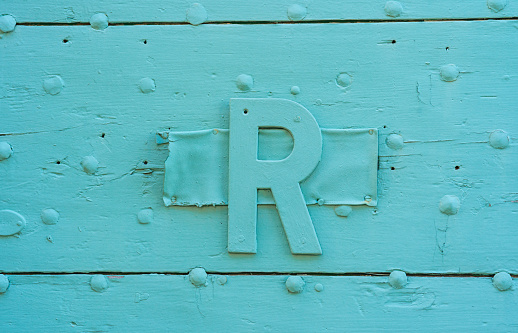 Gros plan sur une lettre R ornant une vieille porte en bois peinte en bleu turquoise clair
