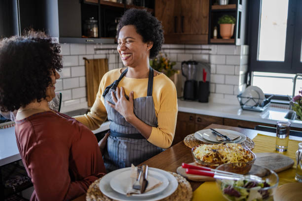 Two woman enjoying lunch at home Portrait of two women enjoying lunch at home. They are having fun in the dining room. gay dinner table stock pictures, royalty-free photos & images