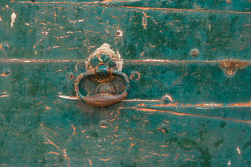 Old rusty door knocker on an old wooden door with cracked dark green paint