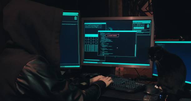 istock Hacker in a hood sits in front of computer screens and hacks databases 1386776737