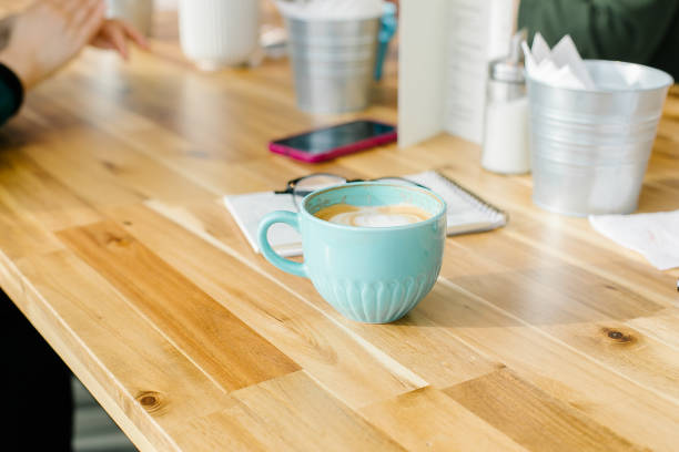 istock Cappuccino coffee in blue cup and eyeglasses, notebook on light table in cafe. 1386776961