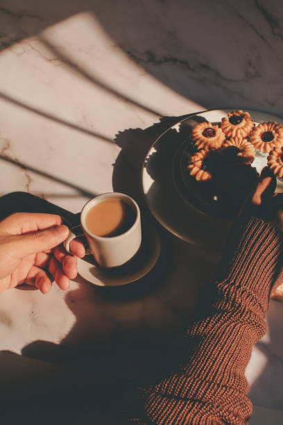 istock Hand holding cookie with jam and hot coffee under morning sun light from window. Autumn warm tone. 1386779011
