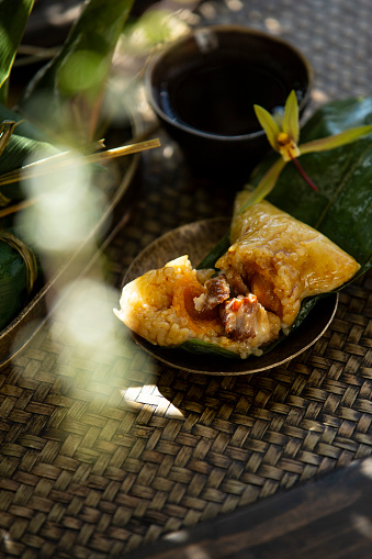 In forest shadows, Salty meat Zongzi is served with a cup of tea on bamboo dinning table.