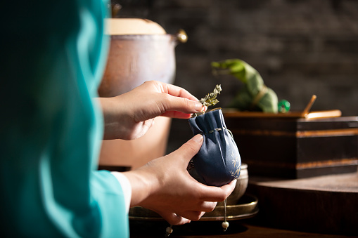 Beside casserole and charcoal stove of kitchen, a Chinese lady is filling wormwood leaves into a silk perfume satchel.