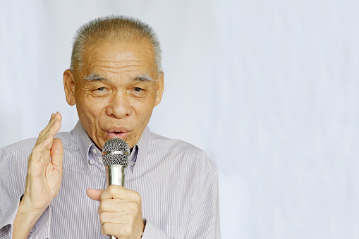 Portrait of an Asian senior man holding microphone while looking at camera.