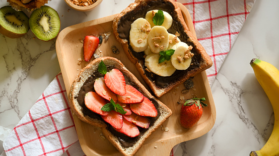 Overhead shot of a healthy fresh fruits toast with homemade dark chocolate spread on wooden plate.