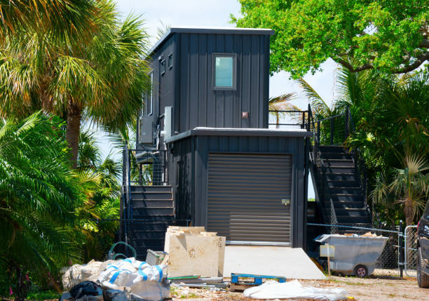 Metal shipping container house under construction on piece of land with lush green trees Metal shipping container house under construction with building material products in front yard on piece of land with lush green trees. tiny house stock pictures, royalty-free photos & images