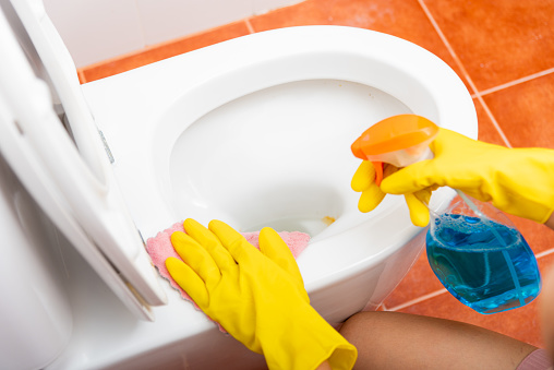 Hand of Asian woman cleaning toilet seat using liquid spray and pink cloth wipe restroom at house, female wearing yellow rubber gloves she sitting cleanup bowl bathroom, Housekeeper healthcare concept