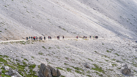 Huge number of hikers are moving along the path at Dolomites in Italy. Italian Alps. Line of people at mountain