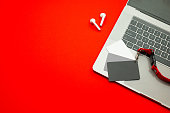 Paris, France - Jan 7, 2022: AirPods wireless Bluetooth headphones created by Apple Computers and of MacBook Pro laptop with gray coupon card on red background