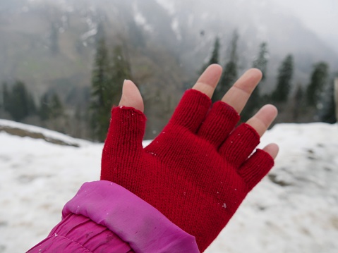 Hand of a girl partially covered in red gloves on a snowy day in the Himalayas.