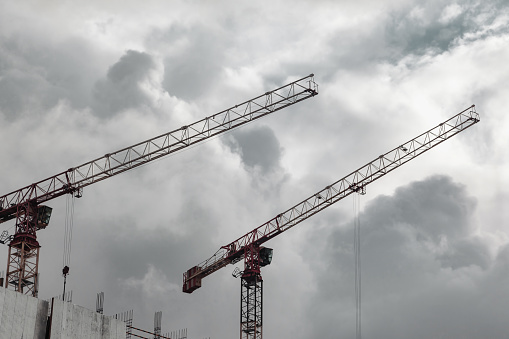 Construction cranes work on creation site against blue sky background. Bottom view of industrial crane. Concept of construction of apartment buildings and renovation of housing. Copy space