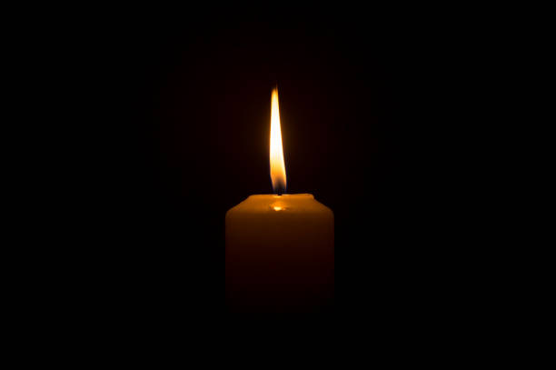 クリスマス、葬儀、または追悼式のために教会のテーブルの上に黒または暗い背景に白いろうそくに輝く単一の燃えるろうそくの炎や光 - candlestick holder single object zen like decoration ストックフォトと画像