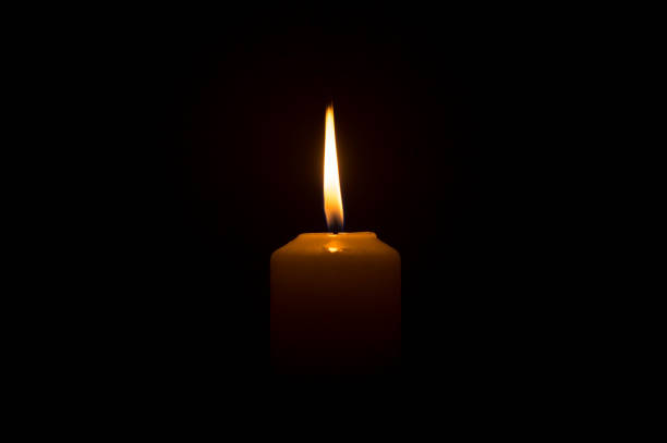 istock A single burning candle flame or light glowing on a white candle on black or dark background on table in church for Christmas, funeral or memorial service 1386815663