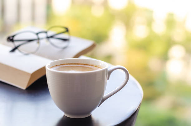 Selective focus of a white cup coffee puts on table at balcony with book and spectacles. Relaxing at home concept.