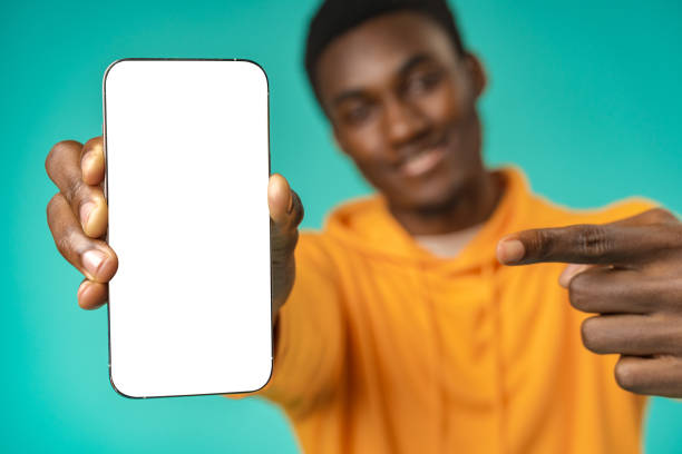 istock Smiling casual black man pointing at blank white cell phone screen in studio 1386816338