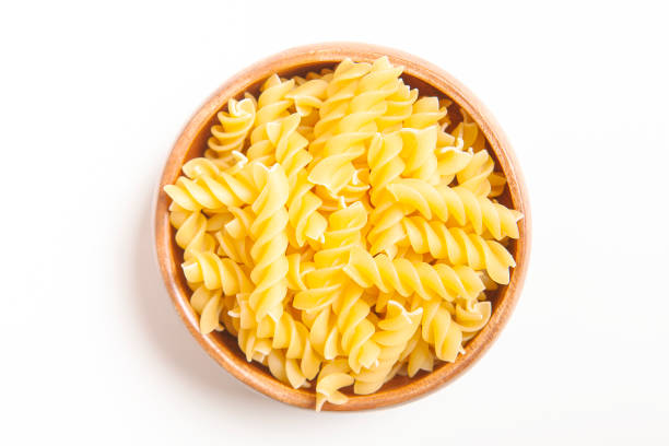 istock Uncooked pasta in wooden bowl on white background. 1386816763