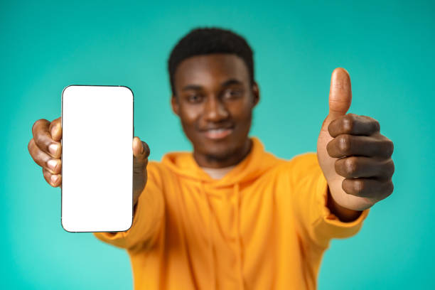 istock Smiling casual black man pointing at blank white cell phone screen in studio 1386819104
