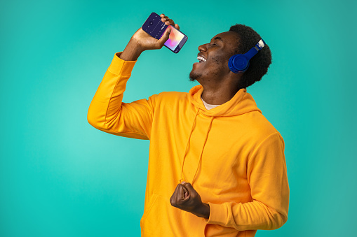 Happy black man listening to music on phone with headphones in mint studio