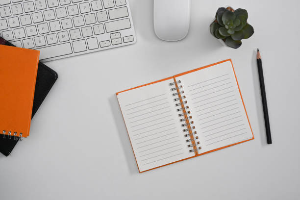istock White office desk with blank notebook, wireless keyboard and potted plant. Top view, flat lay. 1386821701