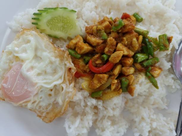 istock Stir-fried chicken with roasted curry paste and sweet basil leaf, lentils mixed vegetables, Fried egg on jasmine rice in white plate on wooden background, thai food. 1386821712