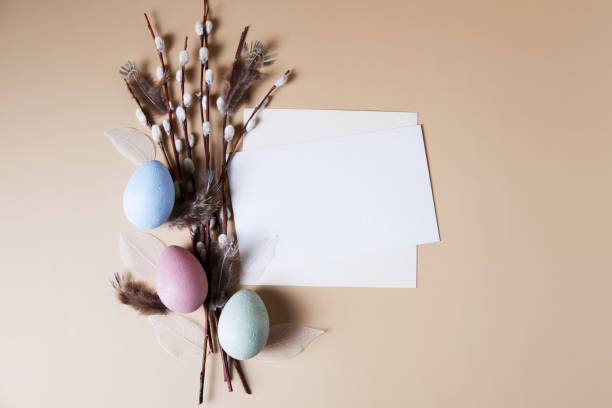istock Multicolored eggs on a beige background next to willow branches and a white sheet for text. 1386822331