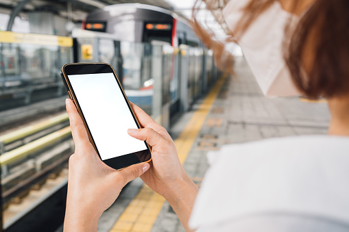 Close up  hand of woman holding a phone with a white screen blank screen  on a metro train  station, People with smartphone  template, commuter, and transportation concept